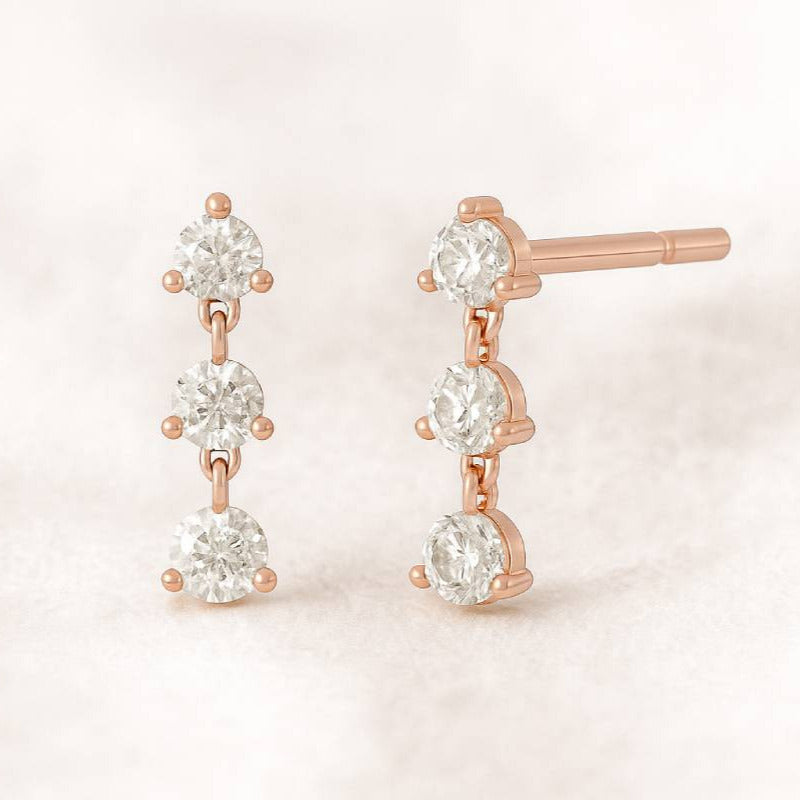 Rose gold earrings with clear gemstones on a light pink background