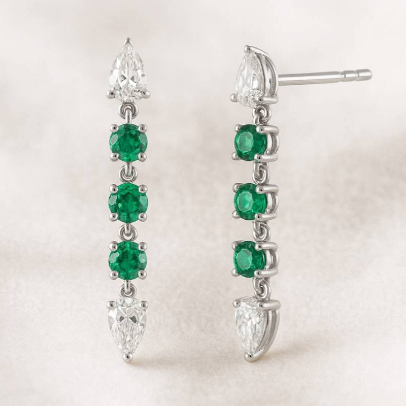 Pair of emerald and diamond earrings on a light background