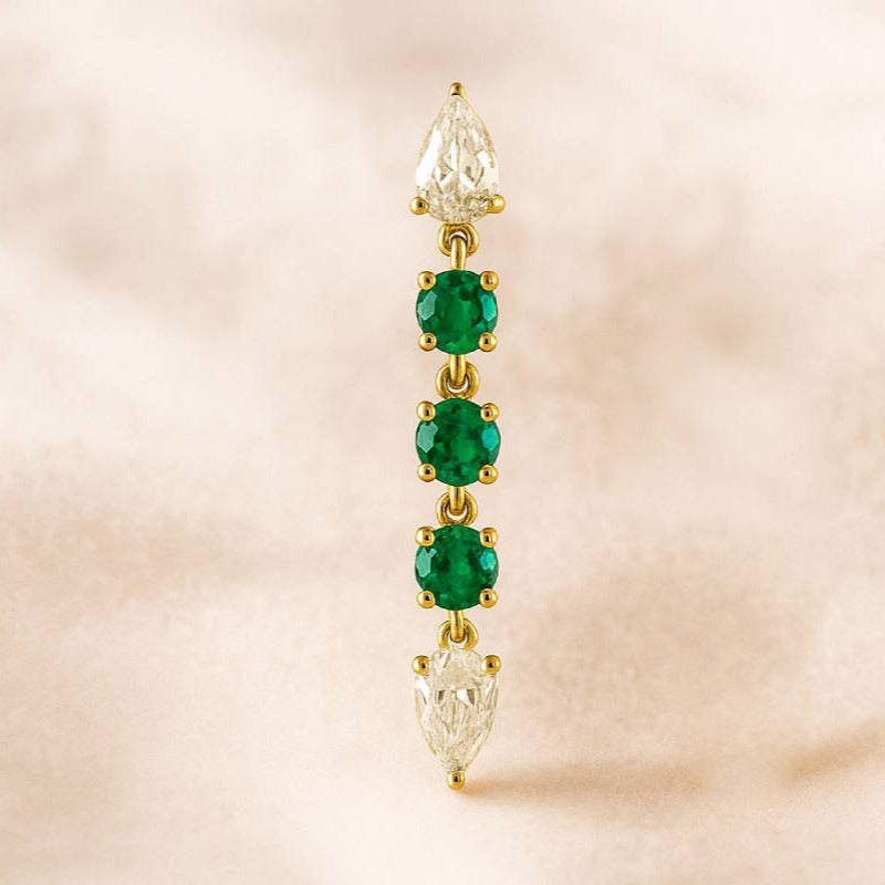 Gold earring with emerald stones on a beige background