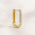 Gold hoop earring with embedded diamonds on a light beige background