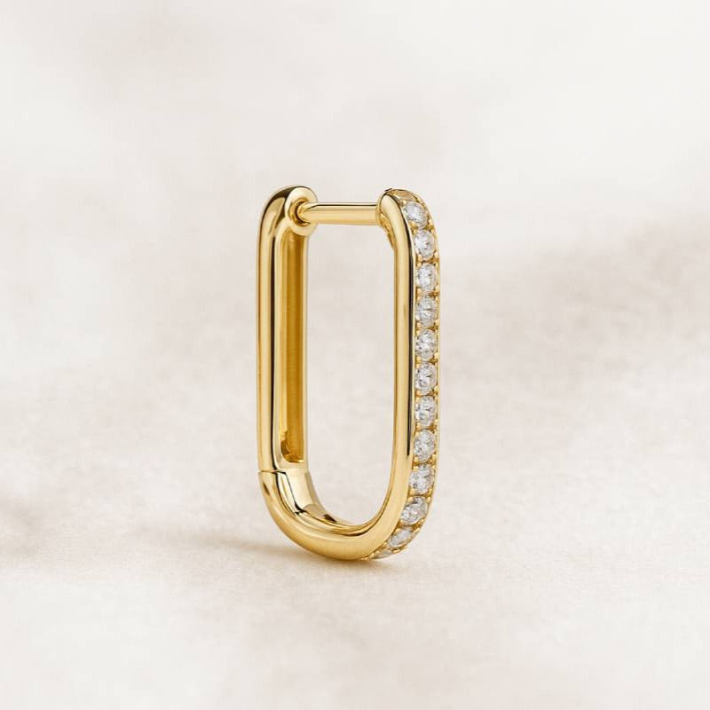 Gold hoop earring with embedded diamonds on a light beige background