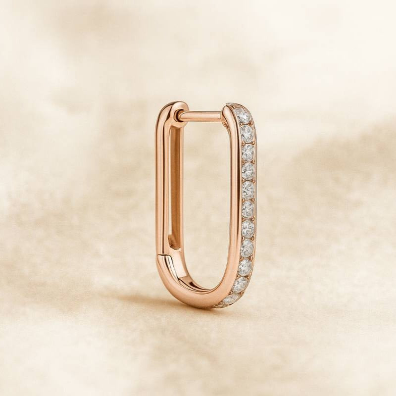 Rose gold hoop earring with embedded diamonds on a beige background