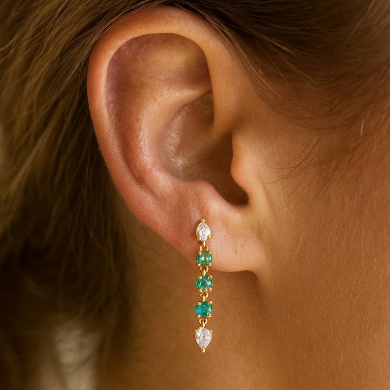 Close-up of an ear wearing a diamond and emerald earring with a blurred background