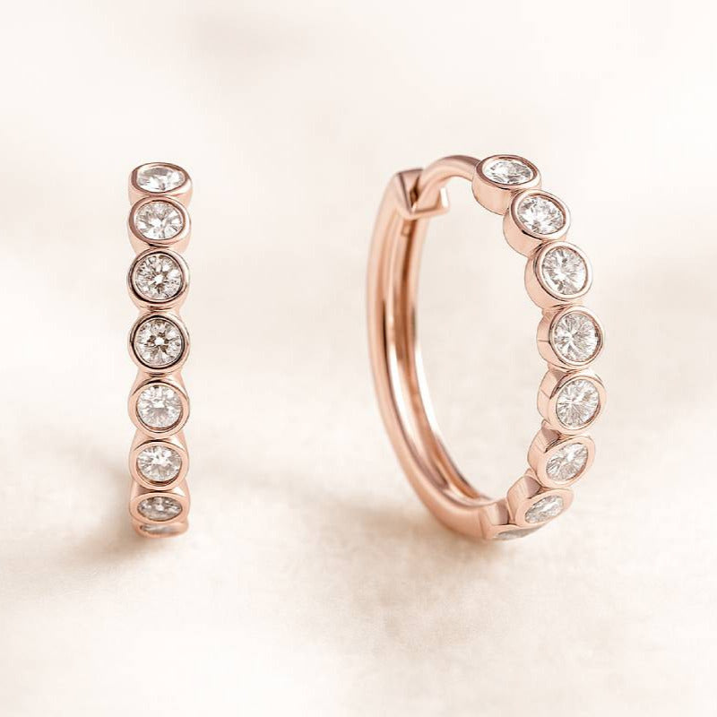 Rose gold hoop earrings with embedded diamonds on a light background