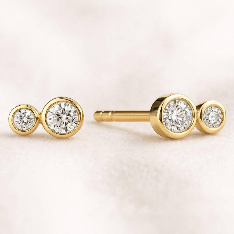 Gold earrings with clear gemstones on a light pink background