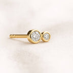 Gold earrings with clear gemstones on a light pink background