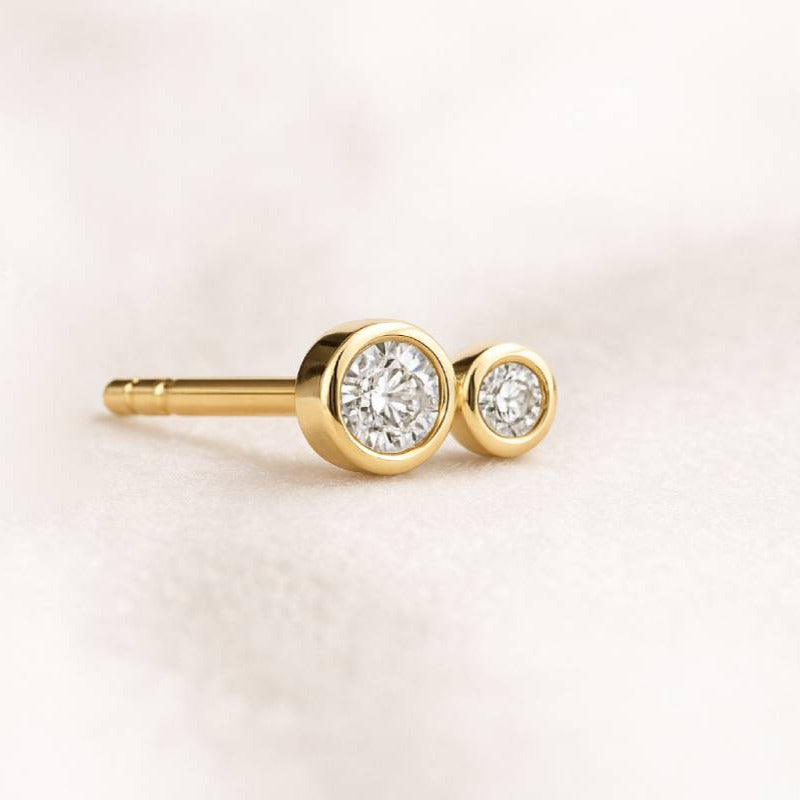 Gold earrings with clear gemstones on a light pink background