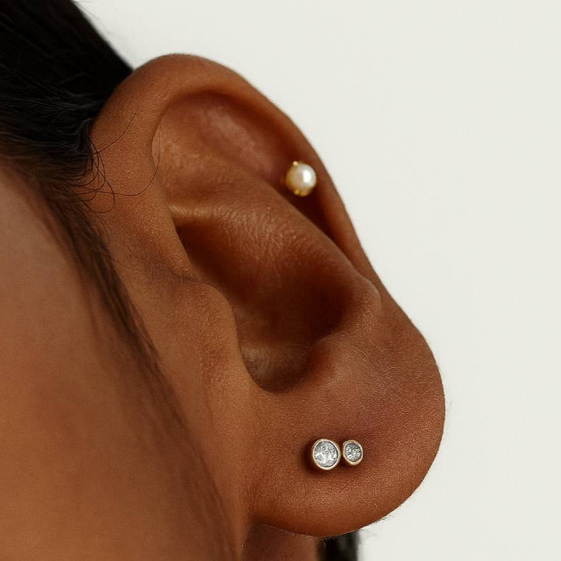 Close-up of an ear with pearl and diamond earrings on a neutral background
