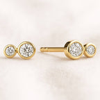 Gold earrings with clear gemstones on a light pink background