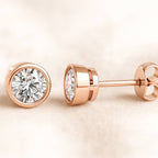 Rose gold diamond stud earrings on a beige background