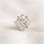 Princess-cut diamond with gold prongs on a light beige background