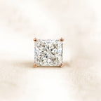Square-cut diamond with rose gold prong setting on a light beige background