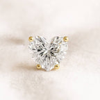 Heart-shaped diamond with gold prongs on a soft beige background