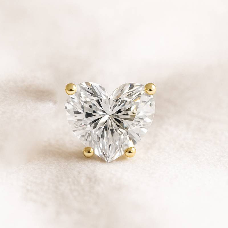 Heart-shaped diamond with gold prongs on a soft beige background