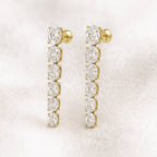 Gold earrings with clear gemstones on a light pink background