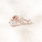 Rose gold earring with three diamonds on a light pink background