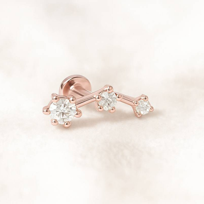 Rose gold earring with three diamonds on a light pink background