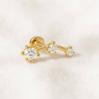 Gold earring with three diamonds on a light pink background