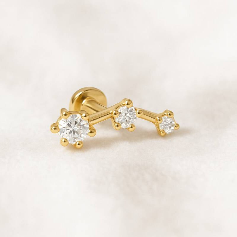 Gold earring with three diamonds on a light pink background