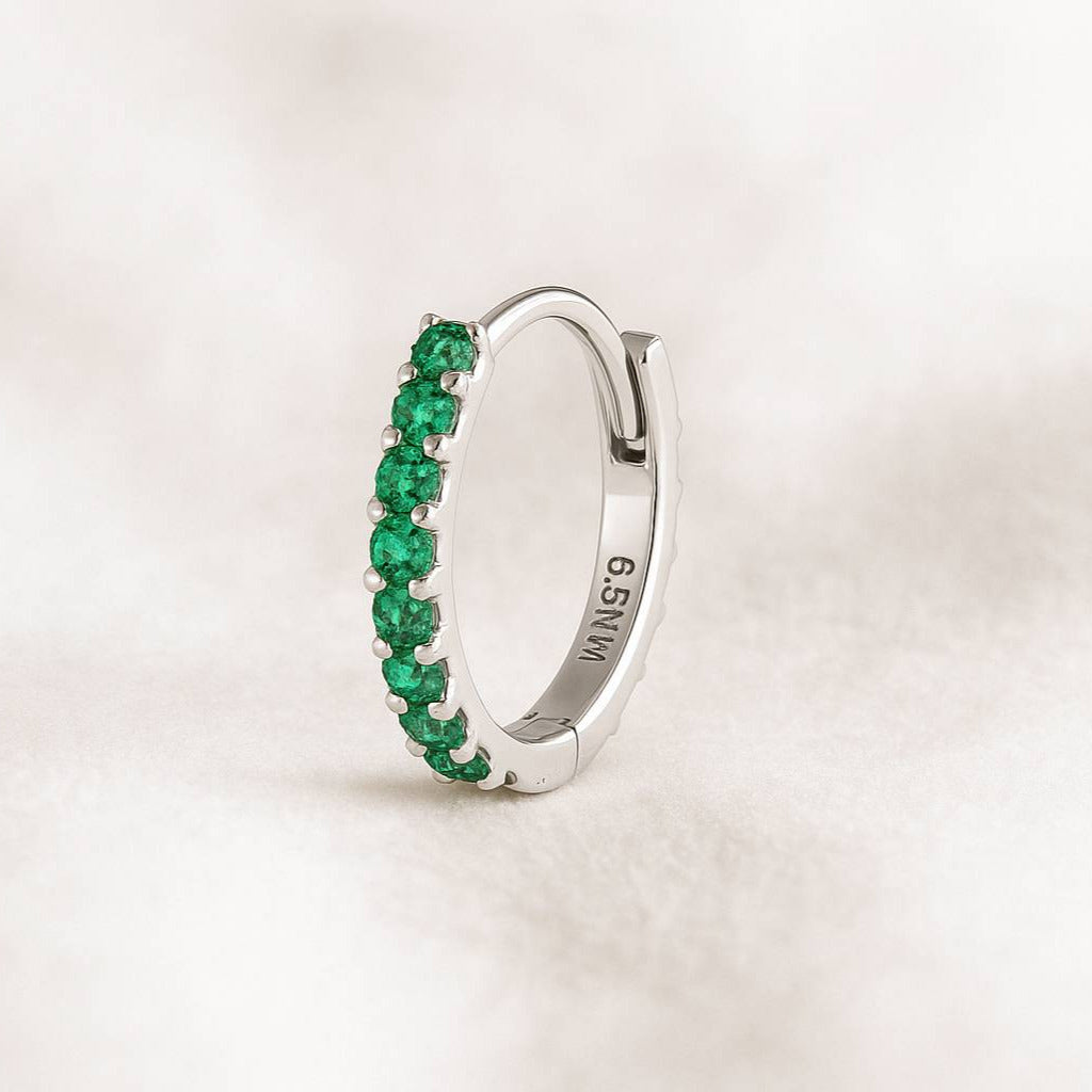 Gold earring with green gemstones on a light beige background