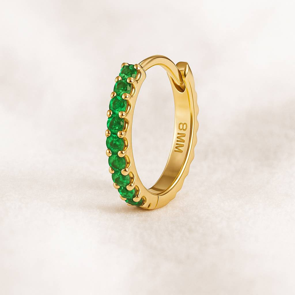 Gold hoop earring with green gemstones on a light beige background