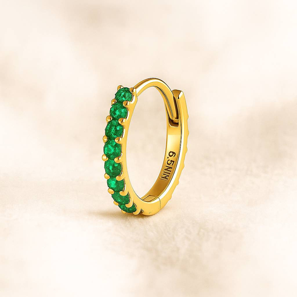 Gold hoop earring with green gemstones on a beige background