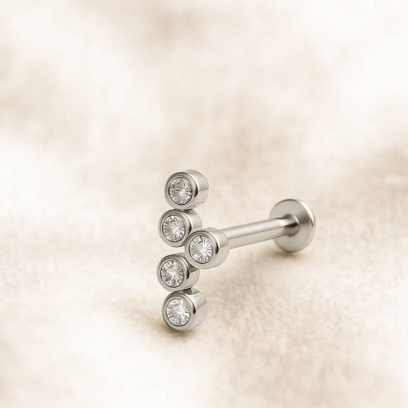 Silver stud earring with clear gemstones on a beige textured background