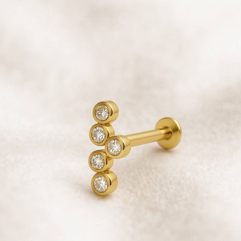 Gold earring with three clear gemstones on a light beige background