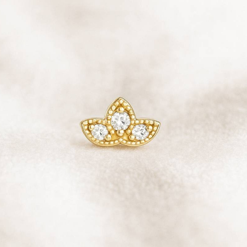 Gold earring with three circular gemstones on a light beige background