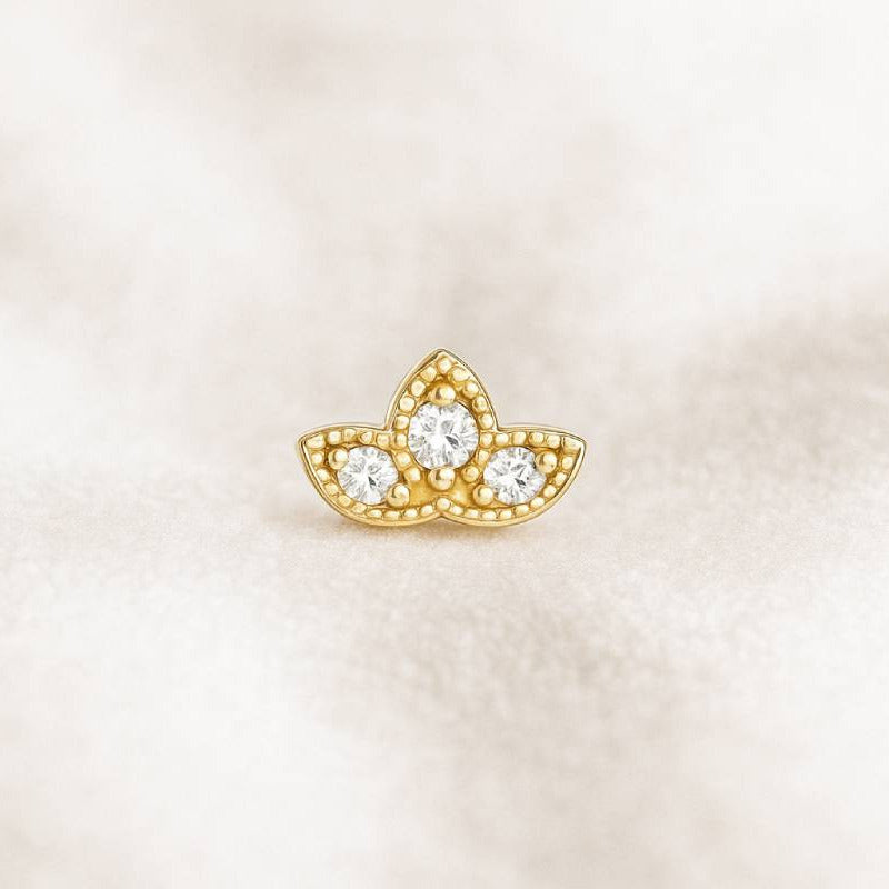 Gold earring with three circular gemstones on a light beige background