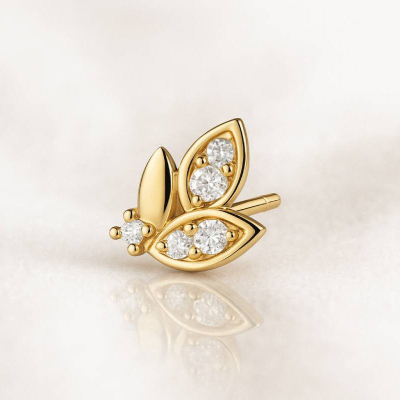 Gold leaf-shaped earring with embedded diamonds on a light background