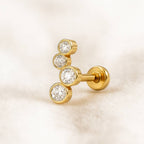 Gold earring with three clear gemstones on a light beige background