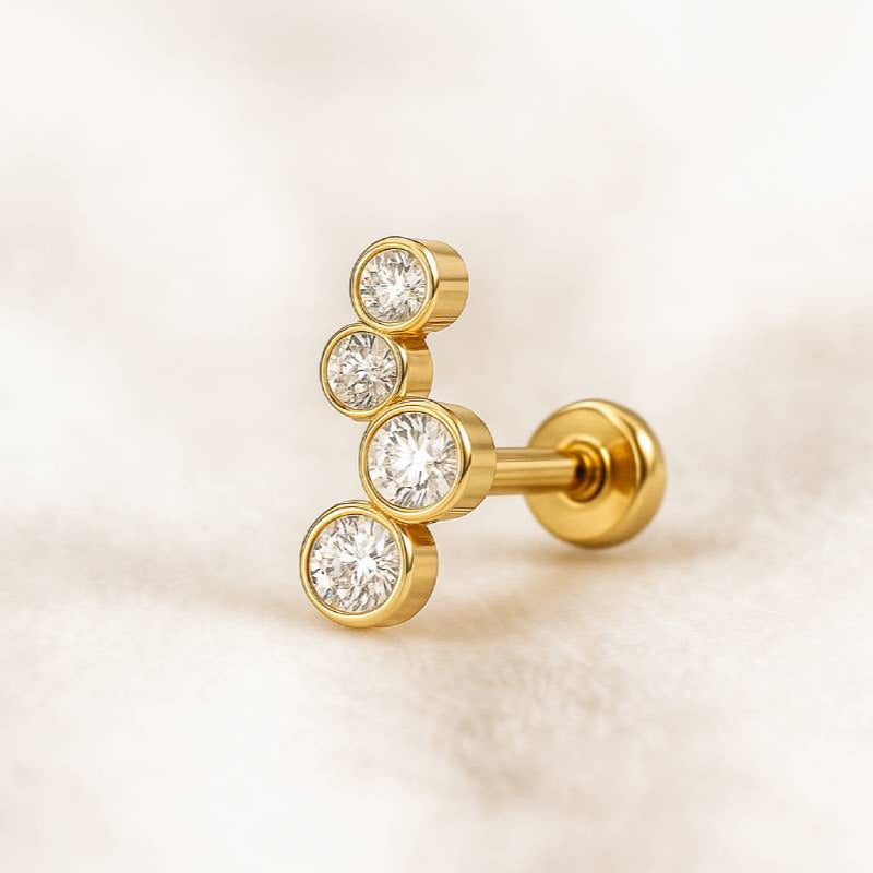 Gold earring with three clear gemstones on a light beige background