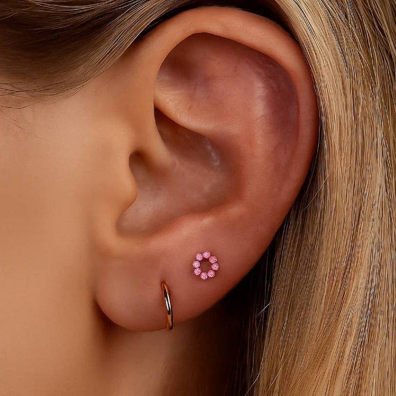 Close-up of an ear wearing a pink flower-shaped earring with a blurred background