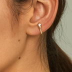 Close-up of an ear wearing a gold earring with a diamond on a neutral background