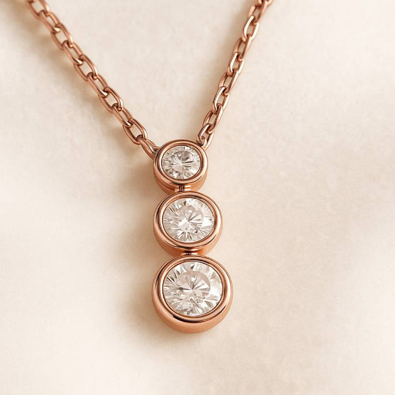 Rose gold necklace with three diamond pendants on a light beige background