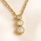 Gold necklace with three diamond pendants on a beige background
