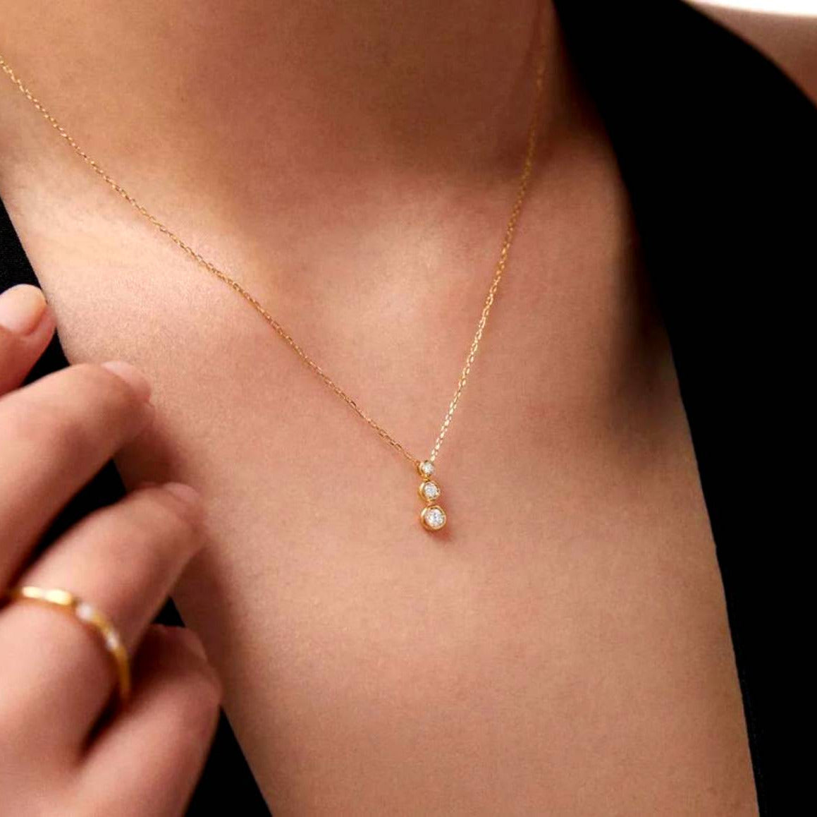 Gold necklace with small pendants on a person's neck against a black background