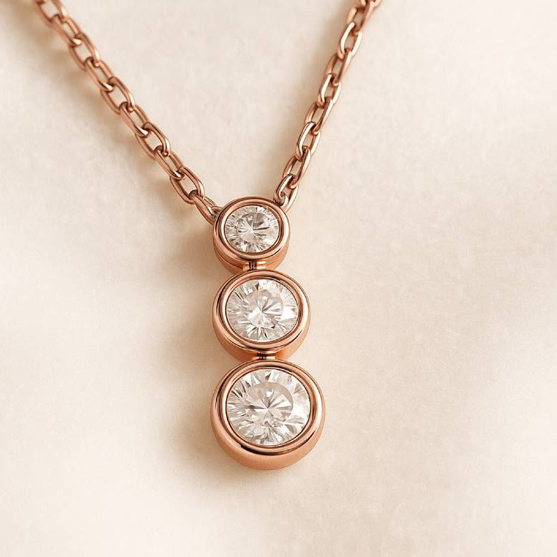 Rose gold necklace with three diamond pendants on a light beige background