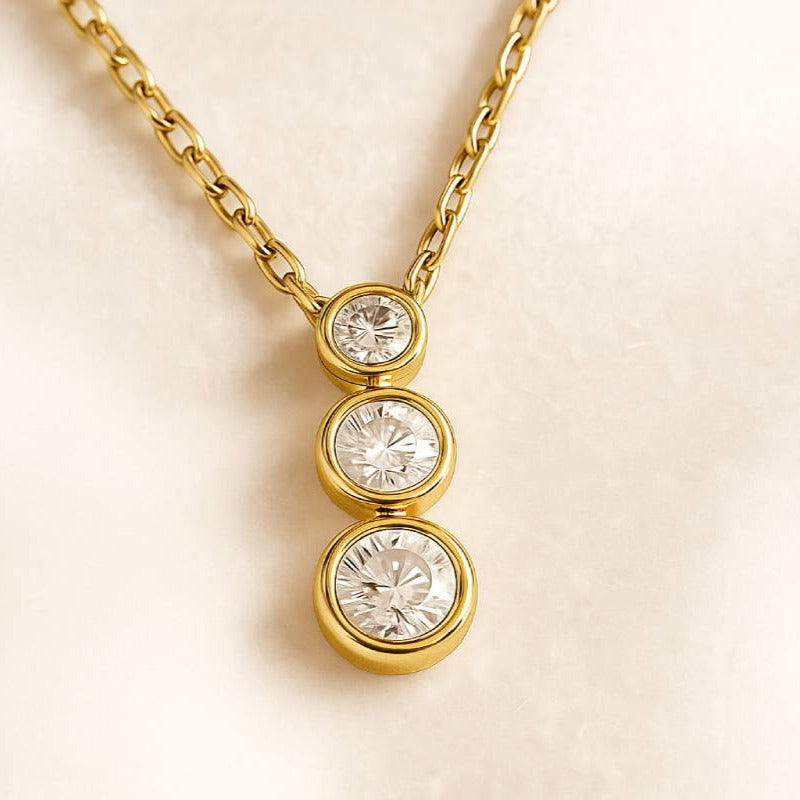 Gold necklace with three diamond pendants on a beige background
