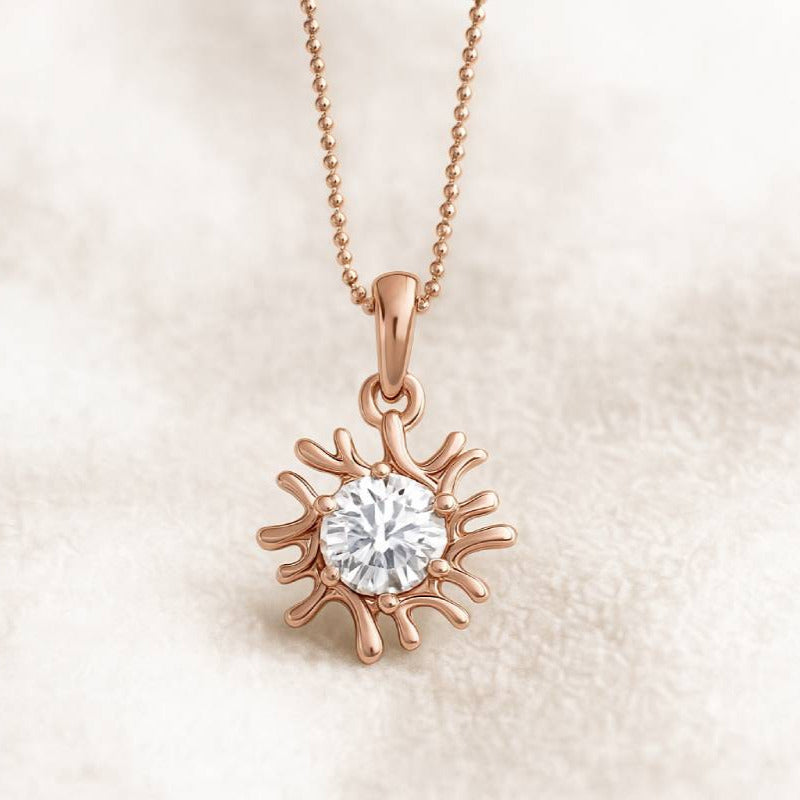 Rose gold sun-shaped pendant with a diamond on a beige background
