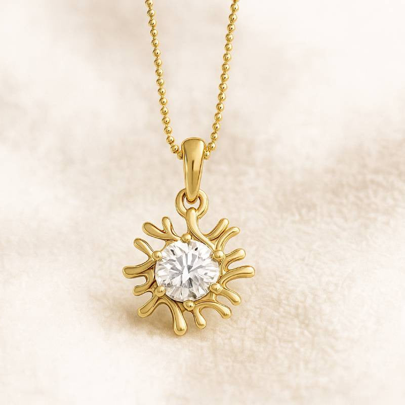 Gold sun-shaped pendant with a diamond on a beige background 