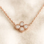 Rose gold necklace with three circular gemstones on a beige background