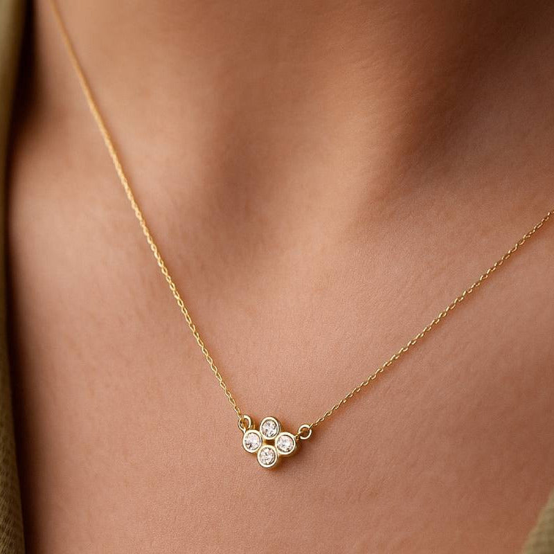 Gold necklace with a clover-shaped pendant on a person wearing a green top.