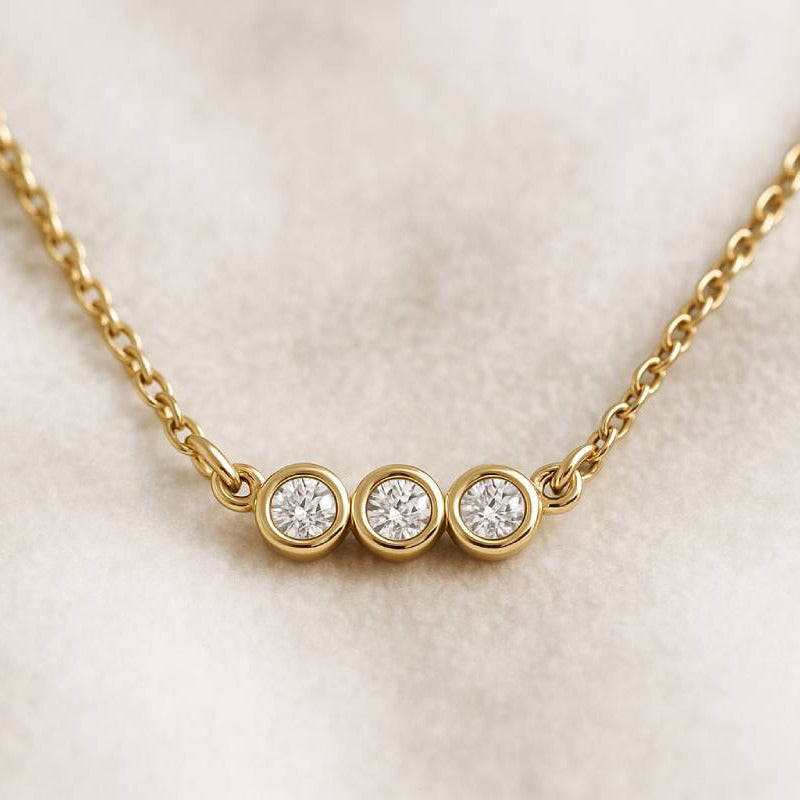 Gold necklace with three diamonds on a light beige background