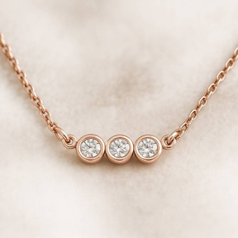 Rose gold necklace with three round diamonds on a light pink background