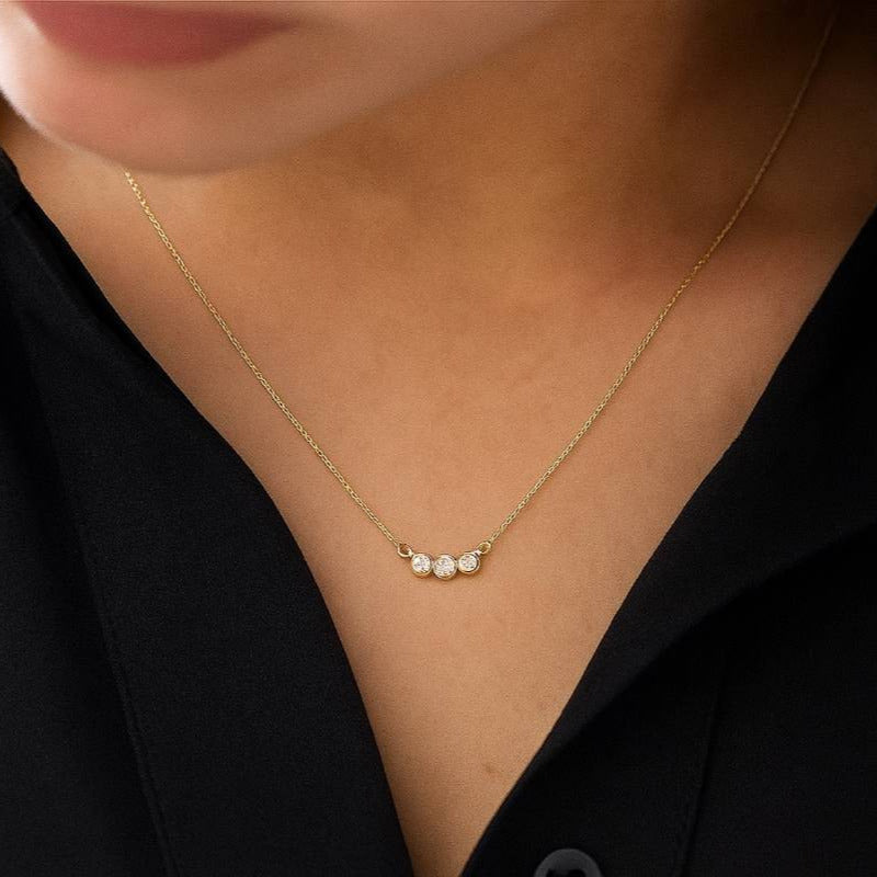 Gold necklace with three small pearls worn by a person against a black background