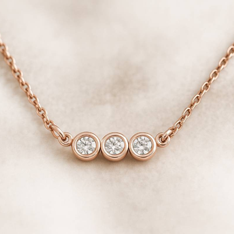 Rose gold necklace with three round diamonds on a light pink background