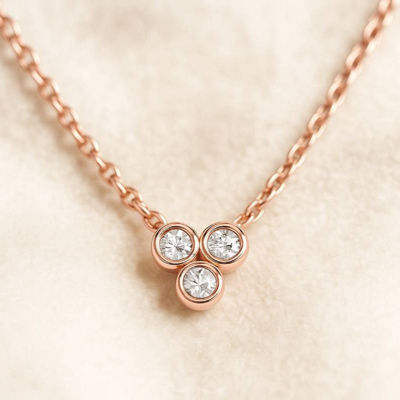 Rose gold necklace with three round diamonds on a beige background