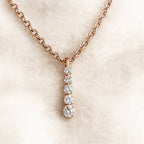 Rose gold necklace with a diamond pendant on a soft beige background